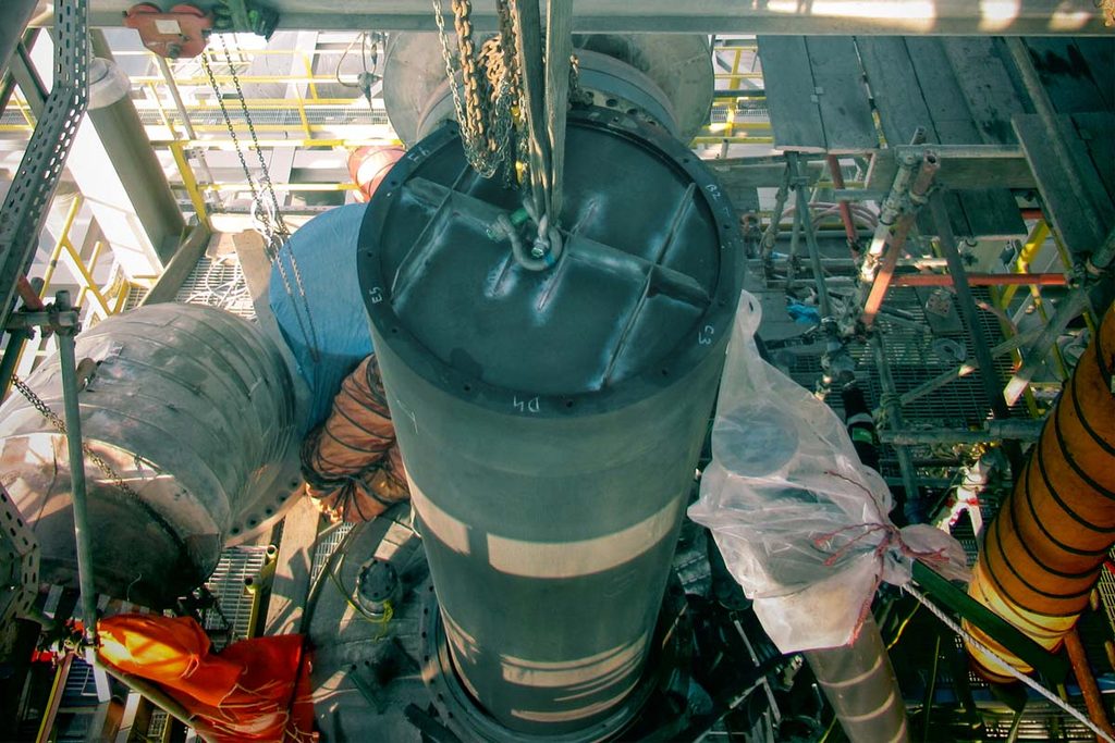 A reactor internal component being lowered into position through the refinery steelwork using chain blocks.